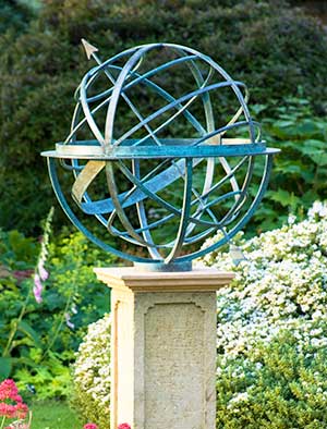 Verdigris bronze armillary sundial on a plinth in an English style garden