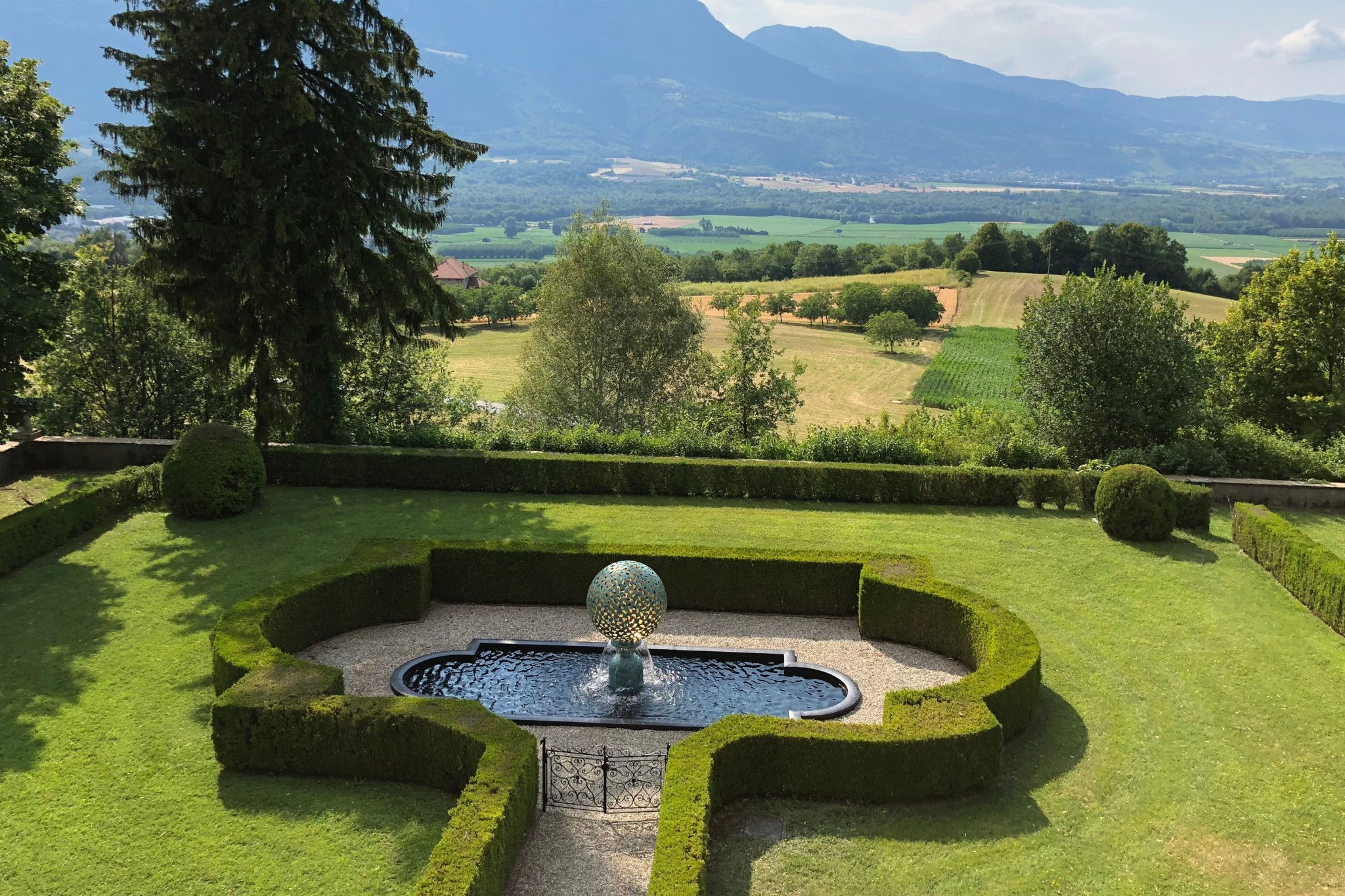 A round water feature stands in a pool in a landscape garden with a view of mountains in the distance.