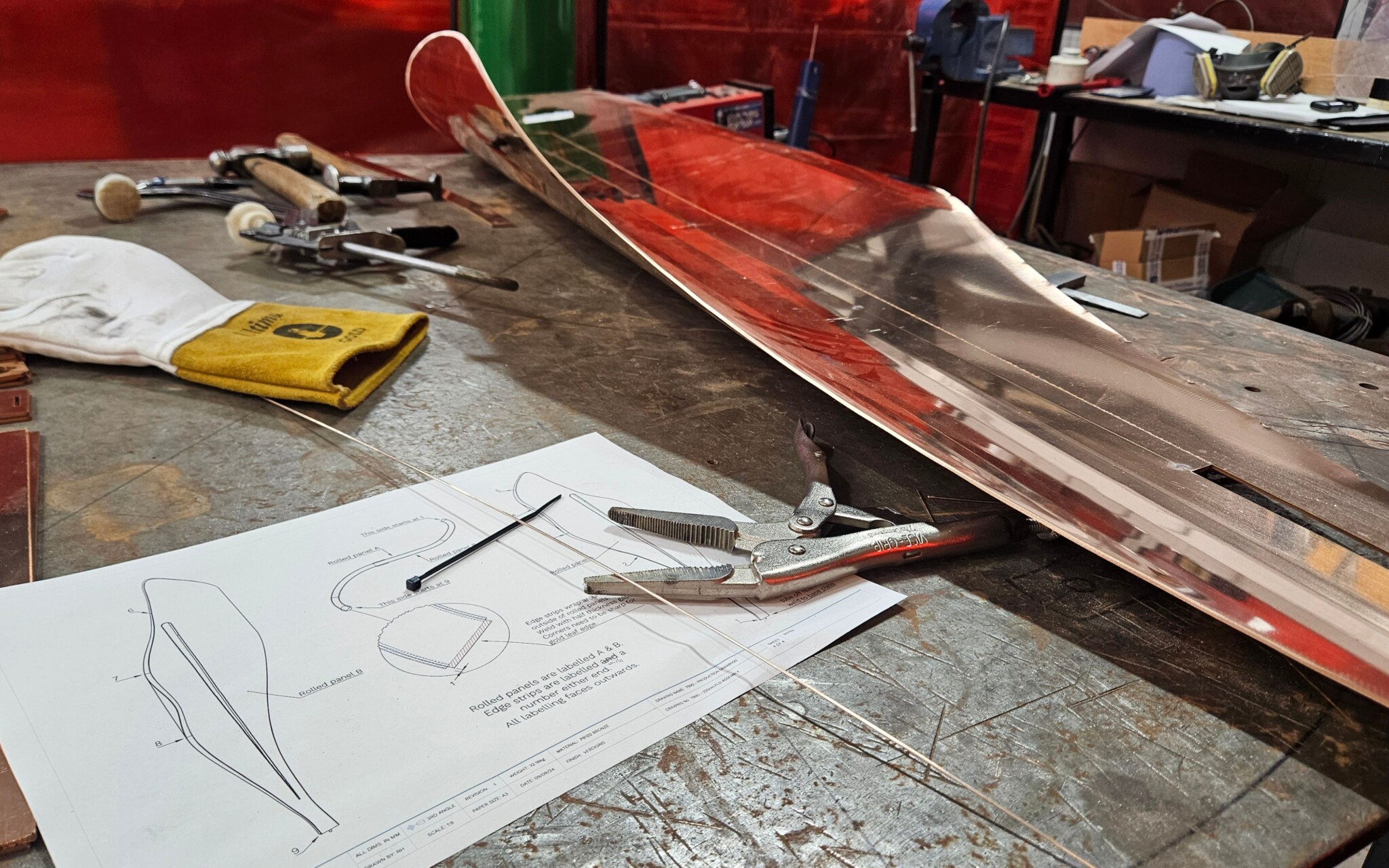 Workbench with an unfinished brass design, drawings and tools