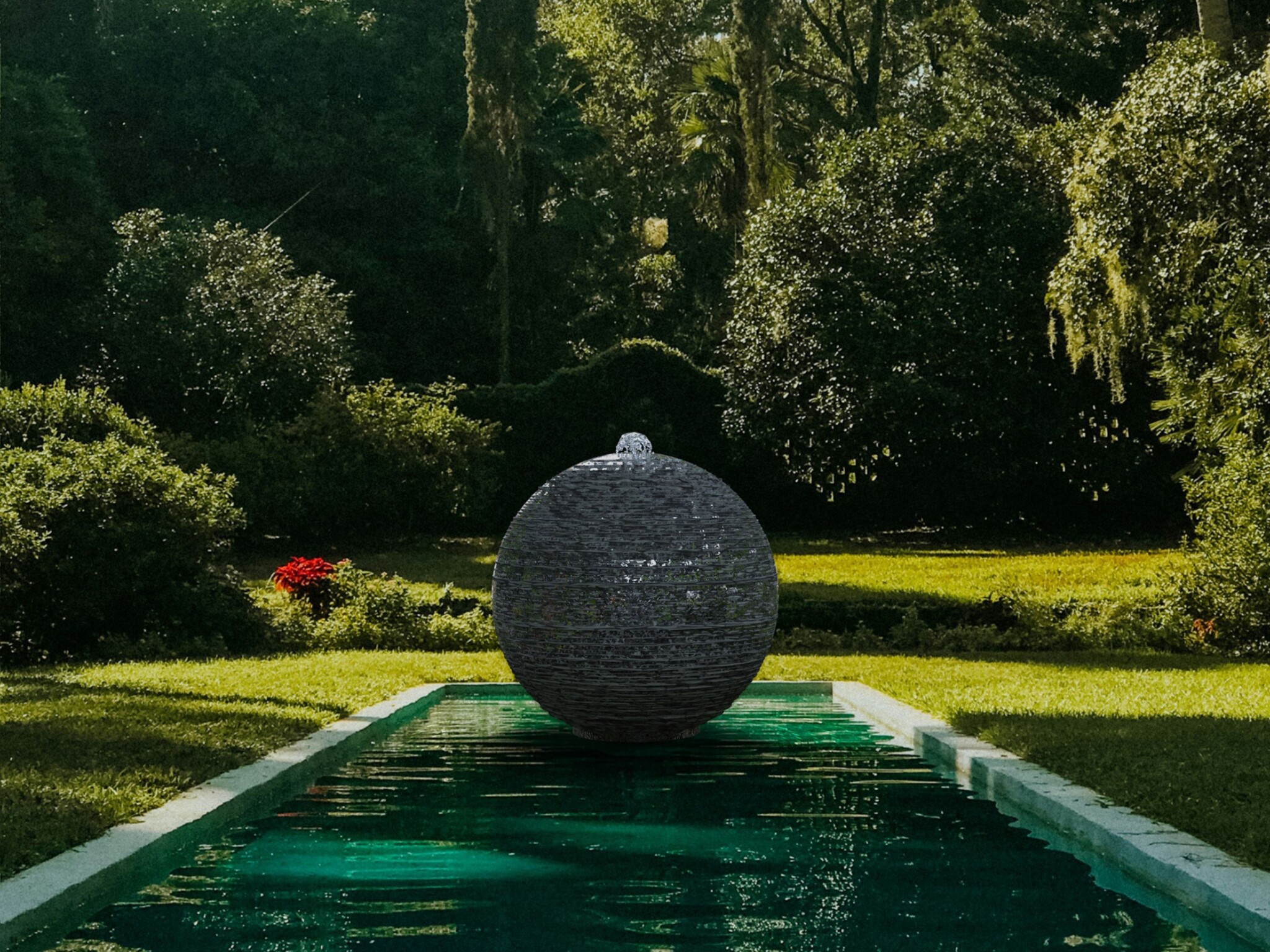 A stone sphere made of slate with a bubbling fountain of water, floating on a pool of water surrounded by woodland gardens