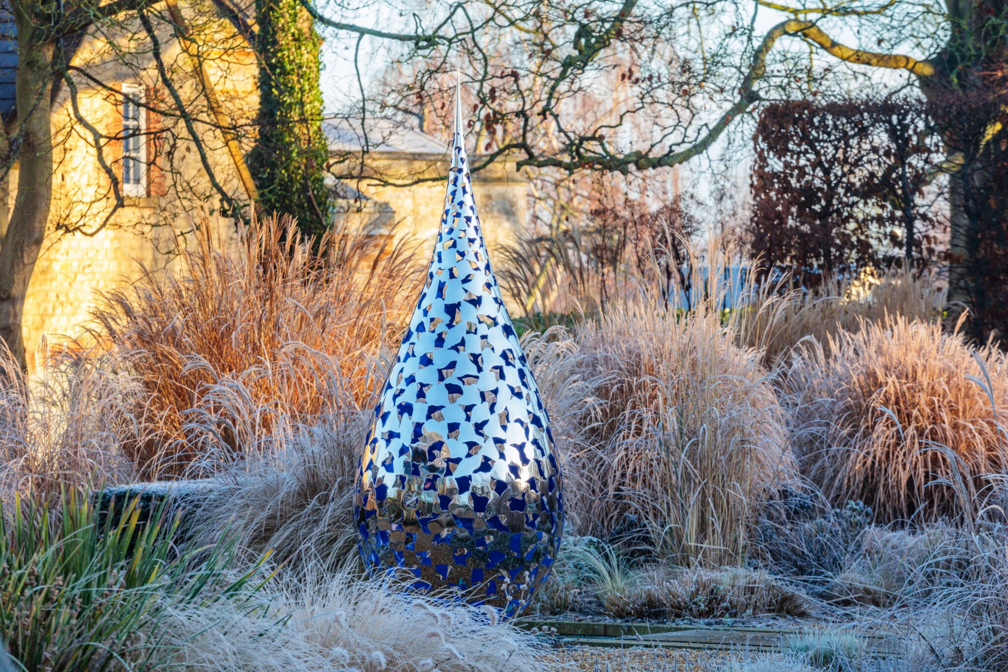 Reflective stainless steel sculpture surrounded by frosty grasses and trees