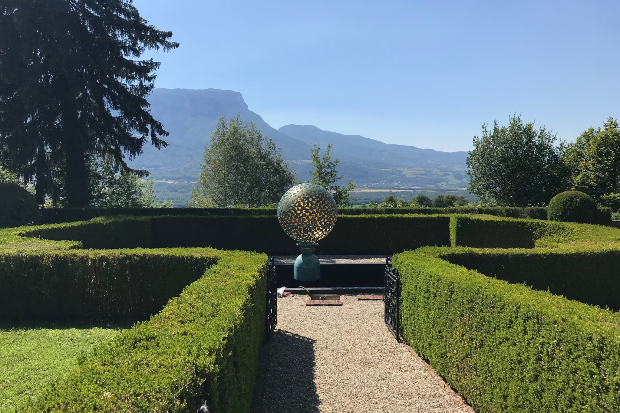 Garden sphere sculpture raised on a garden plinth over a pool draws the eye to the mountain range in the distance.