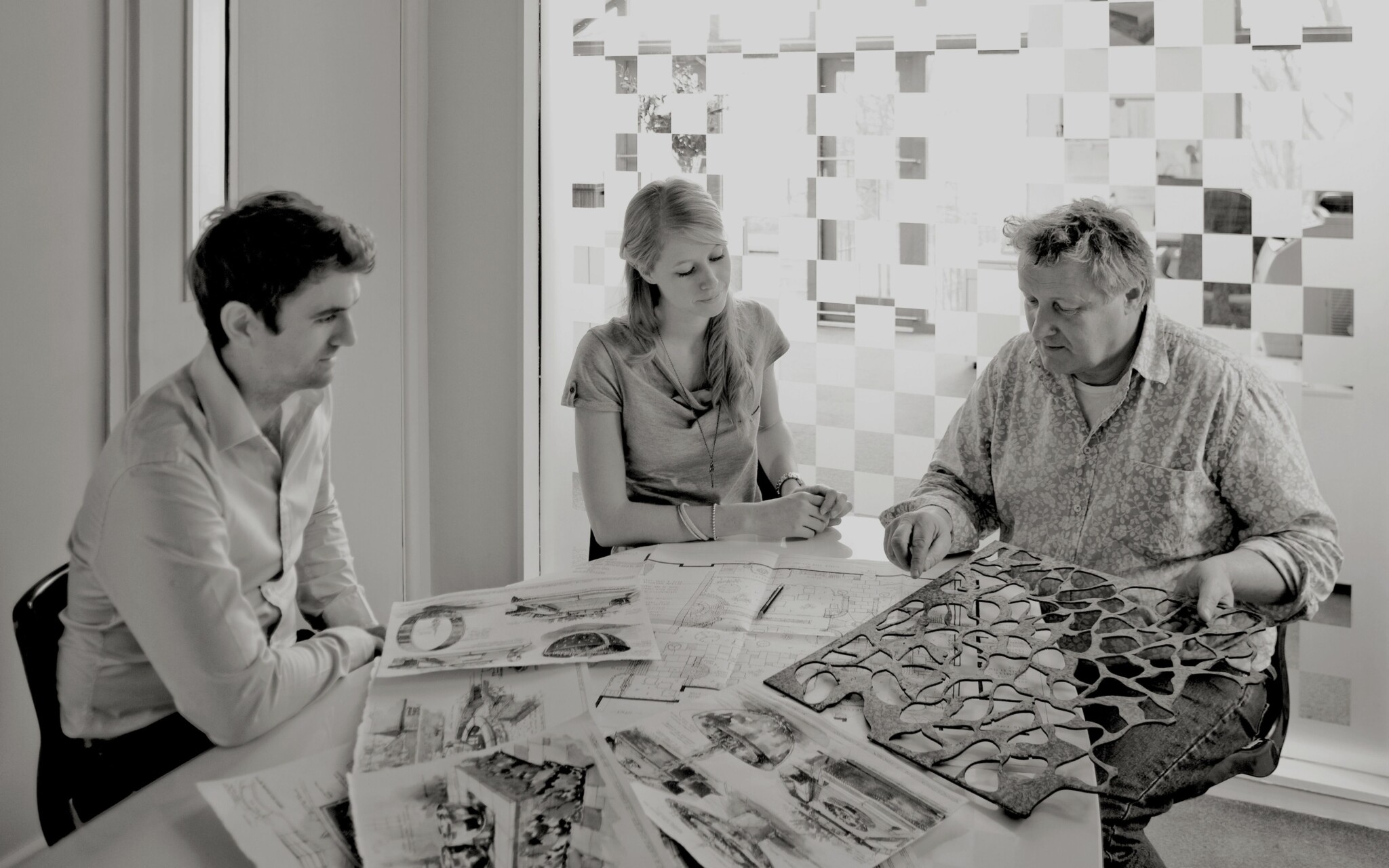 Black & white photo of three people around a table discussing design concepts