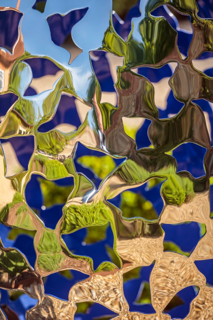 Close up of a shiny stainless steel sculputre with delicate organic cut outs that reveal a vibrant blue, painted interior