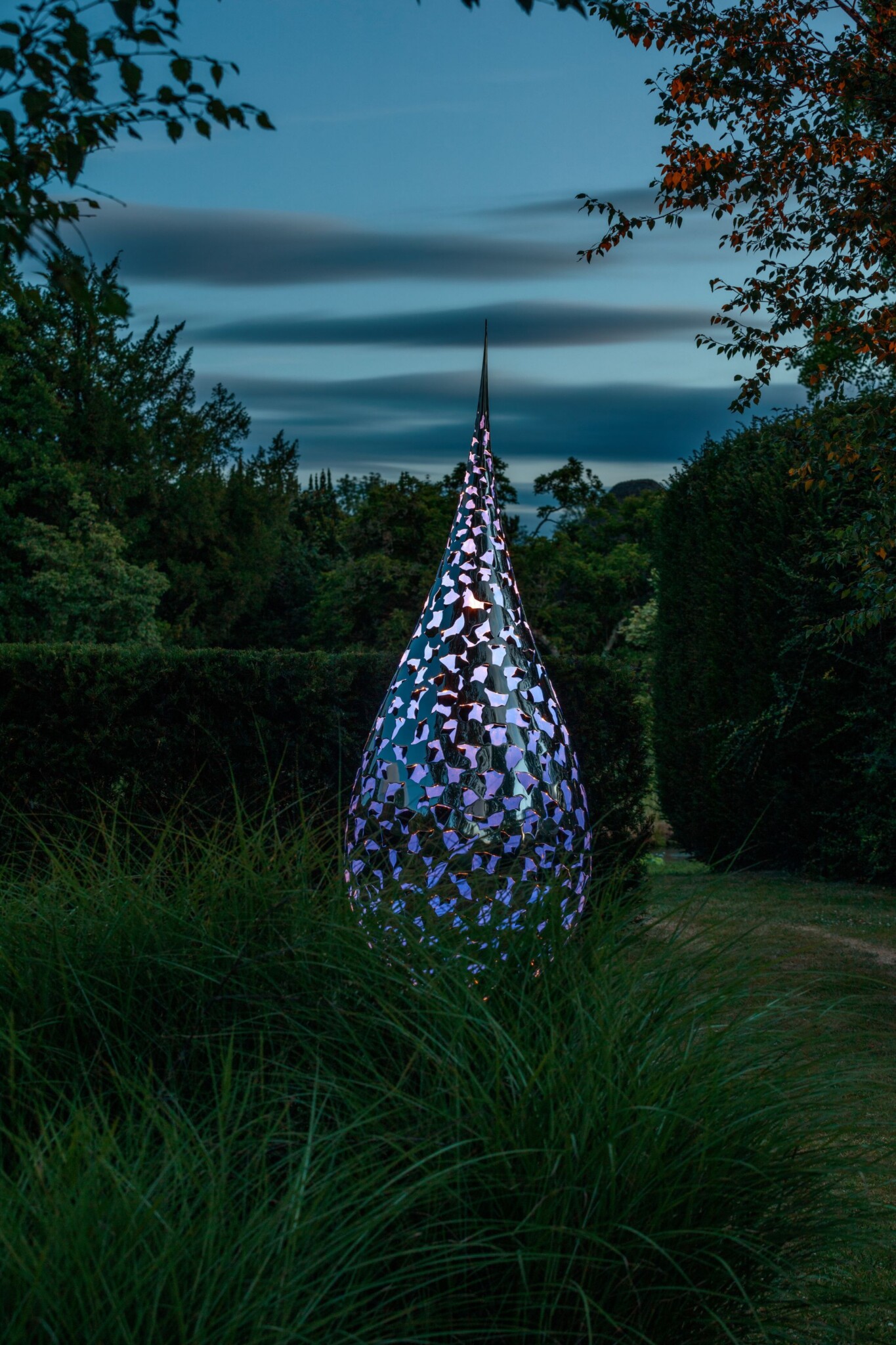 An elegant metal sculpture lit with an LED light glows in the shadowy light of dusk