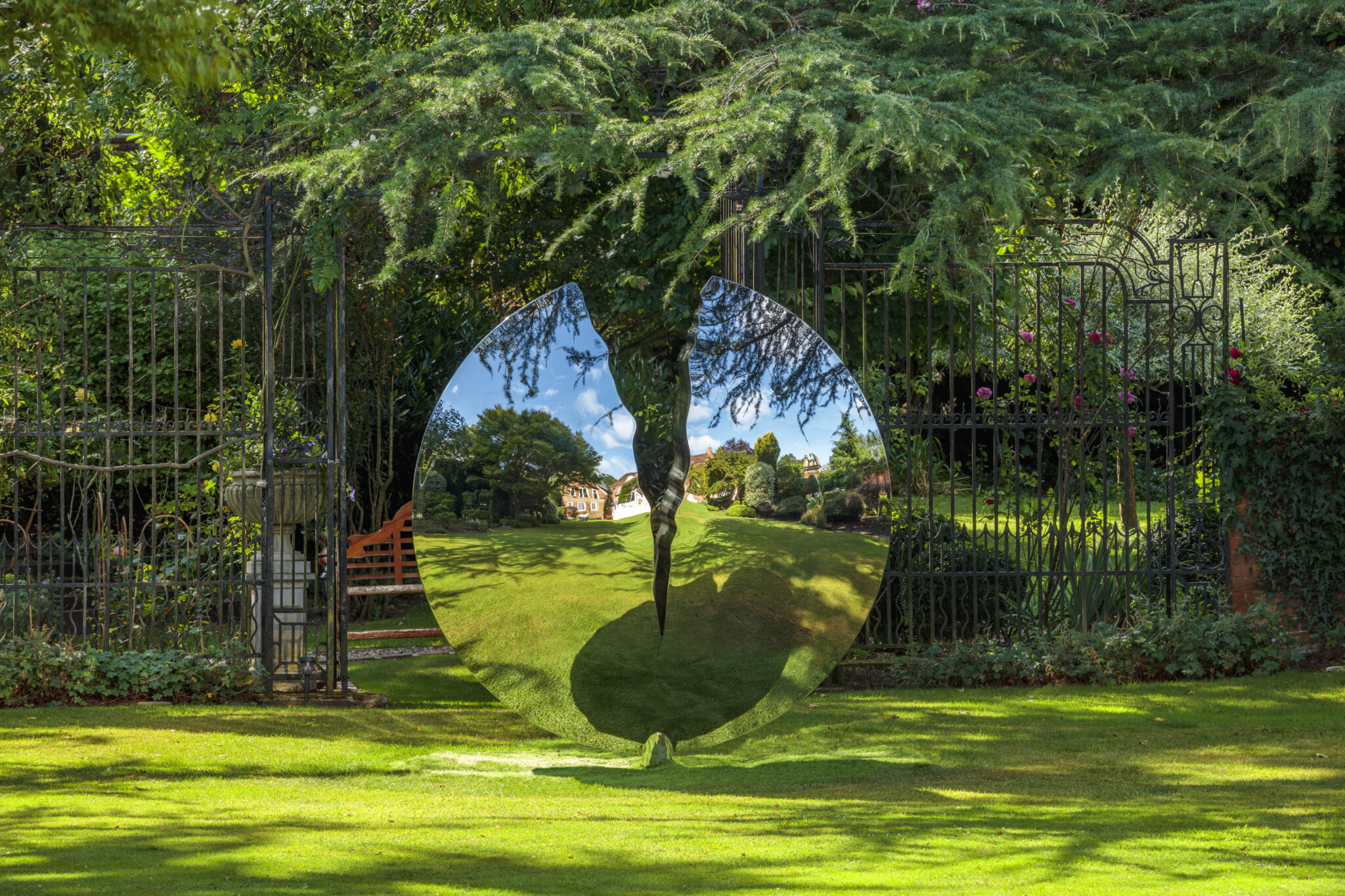 Stainless steel sphere sculpture reflecting surrounding garden and architecture.