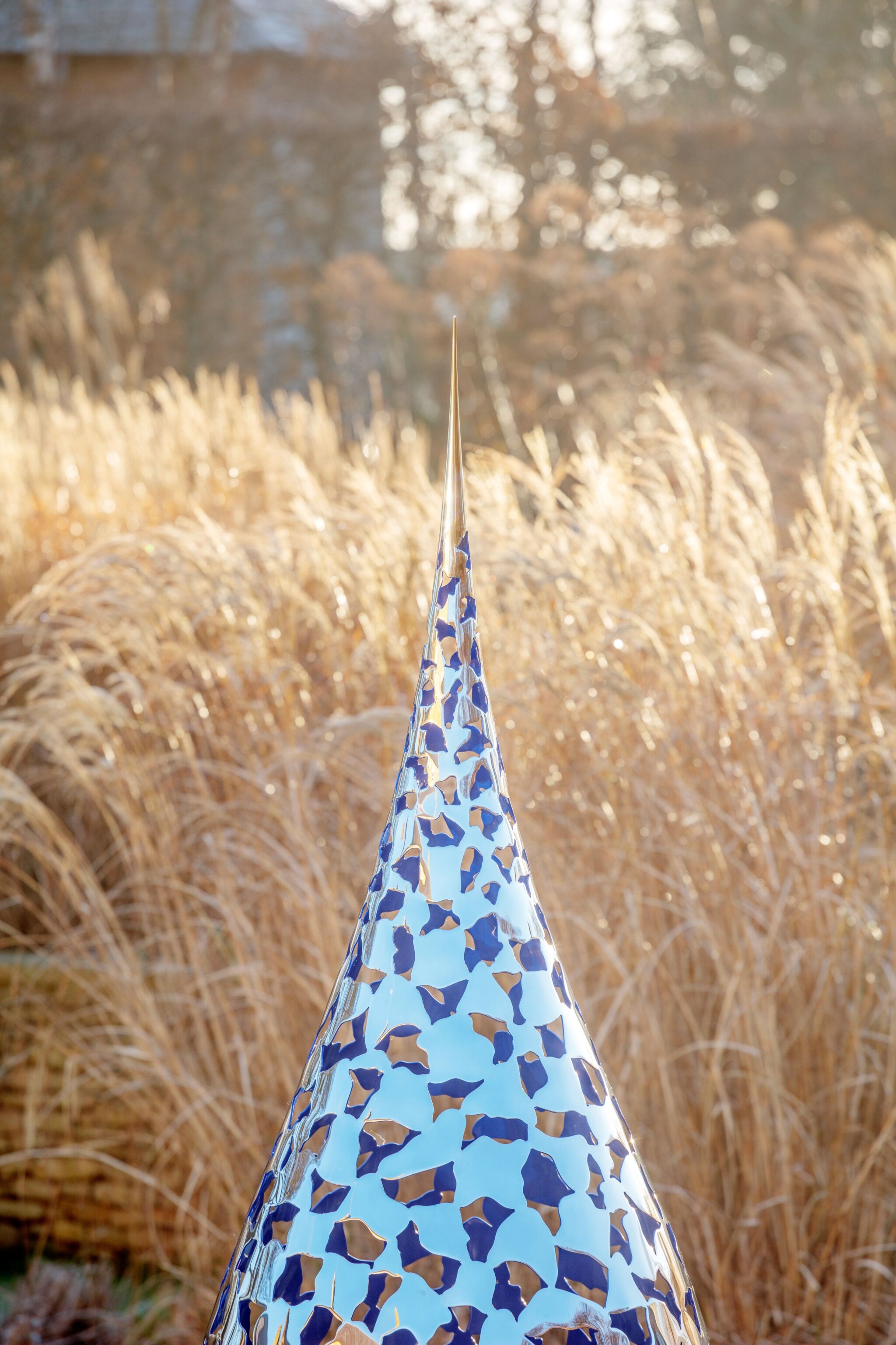 Teardrop bespoke contemporary sculpture with blue and tan mosaic stands before tall, golden grass in sunlight.