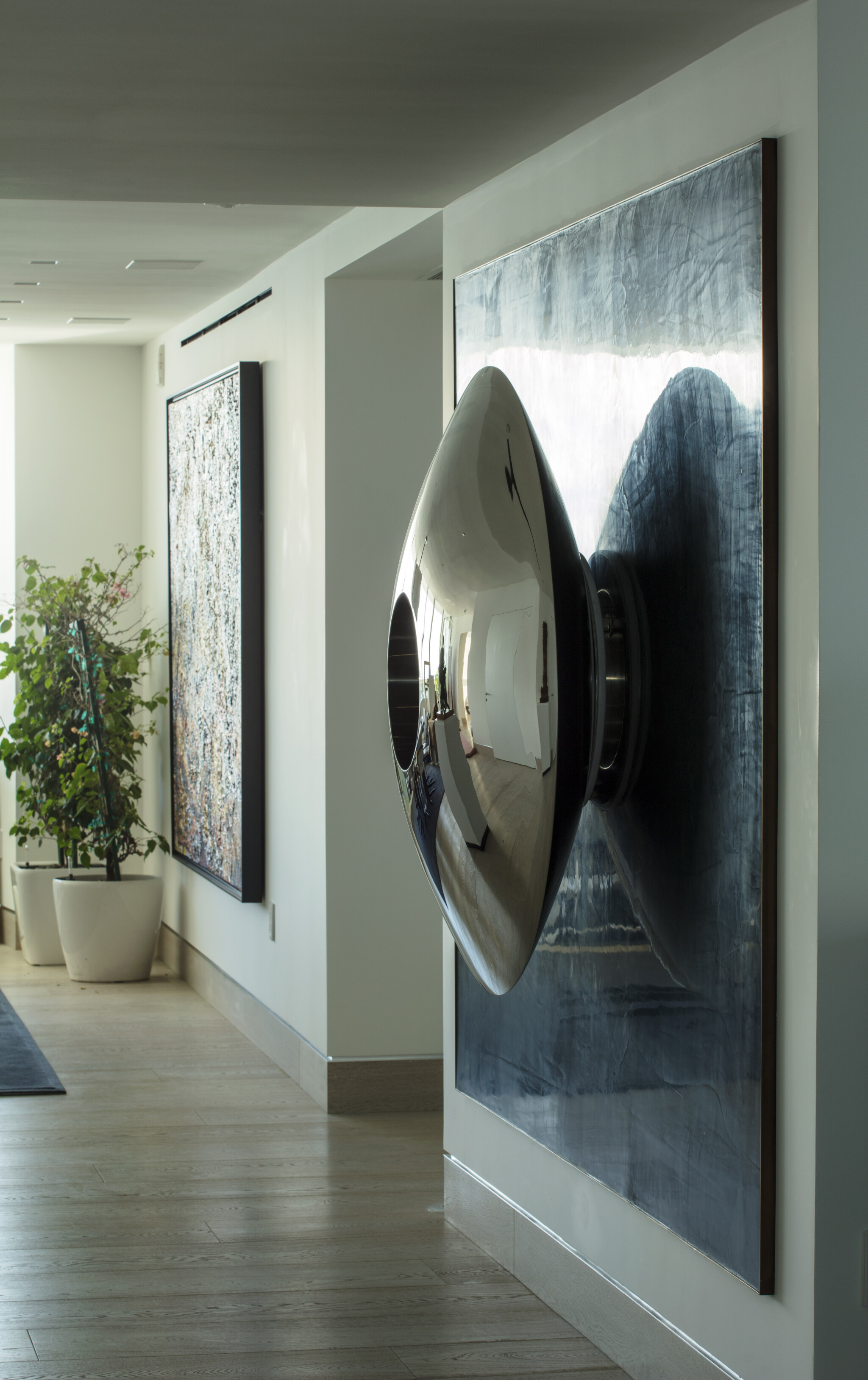 A shiny, metallic, cone-shaped sculpture is mounted on a wall—perfect for hallway sculpture ideas in modern spaces.