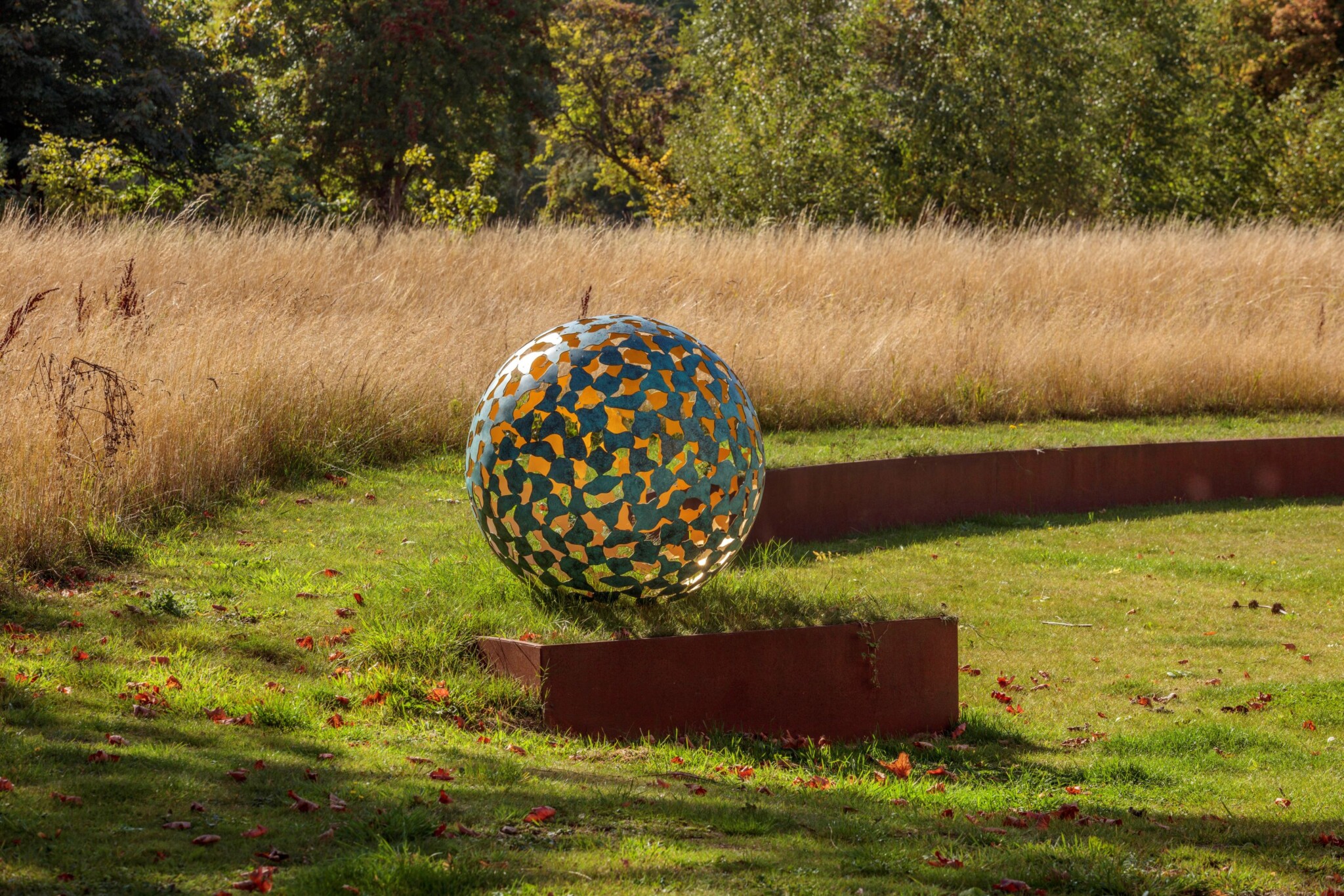 Mantle II in bronze and gold leaf, a contemporary abstract sculpture, stands near a field of tall, dry yellow grass.