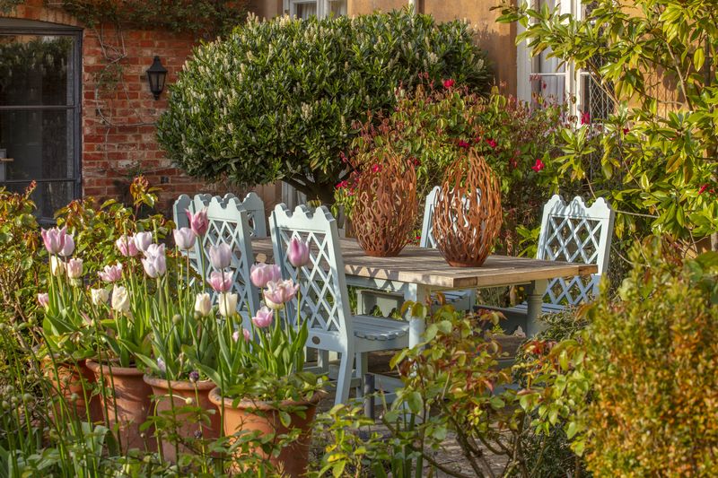 Pastel chairs and a table with vases in a blooming garden offer beautiful courtyard garden ideas among lush greenery.