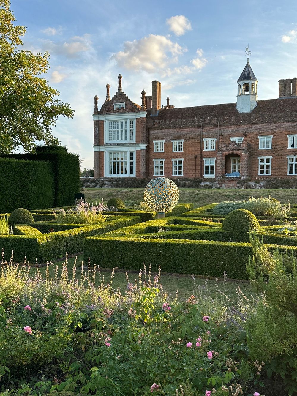 manicured knot garden leading towards a historic brick manor house