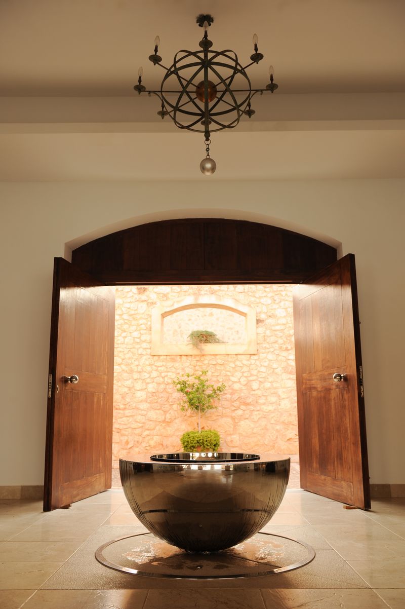 A modern indoor water fountain, perfect for hallway sculpture ideas, stands beneath a geometric chandelier by sunlit doors.