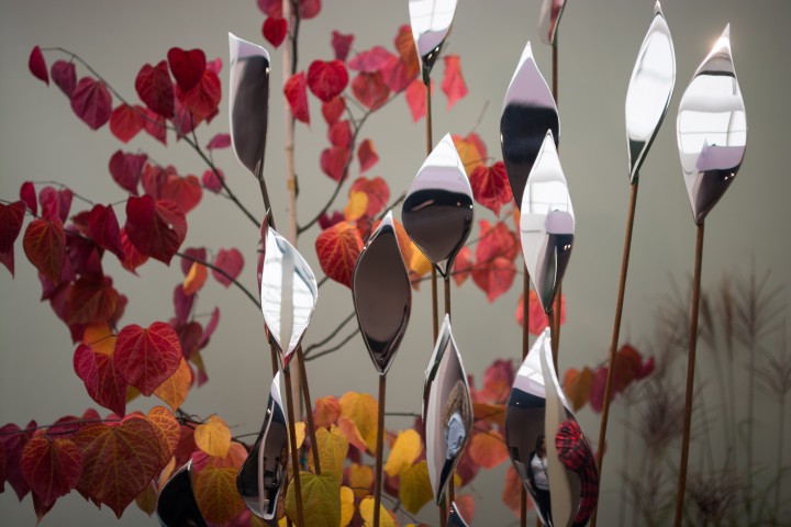 Quiver stainless steel leaf sculptures stand among red and orange autumn leaves against a neutral background.