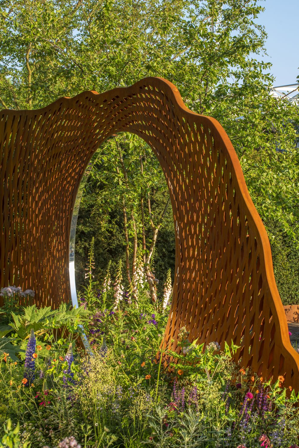 Curved wooden sculpture with oval opening, surrounded by flowers—unique copper garden sculpture ideas for vibrant gardens.