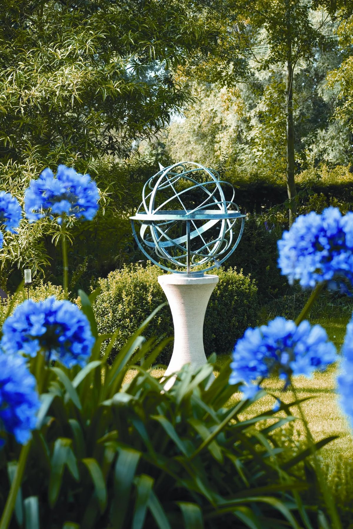 A metal armillary sphere on a plinth, surrounded by vibrant blue flowers—perfect for garden sundial ideas.