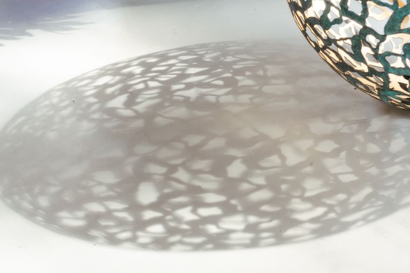 Decorative metal bowl casting intricate, leafy shadows—perfect for unique hallway sculpture ideas in sunlight.