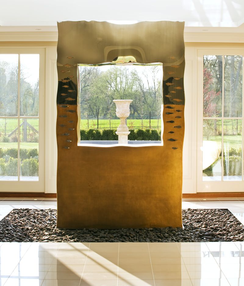 A modern bronze sculpture frames a white urn, perfect for hallway sculpture ideas with views of a green garden.