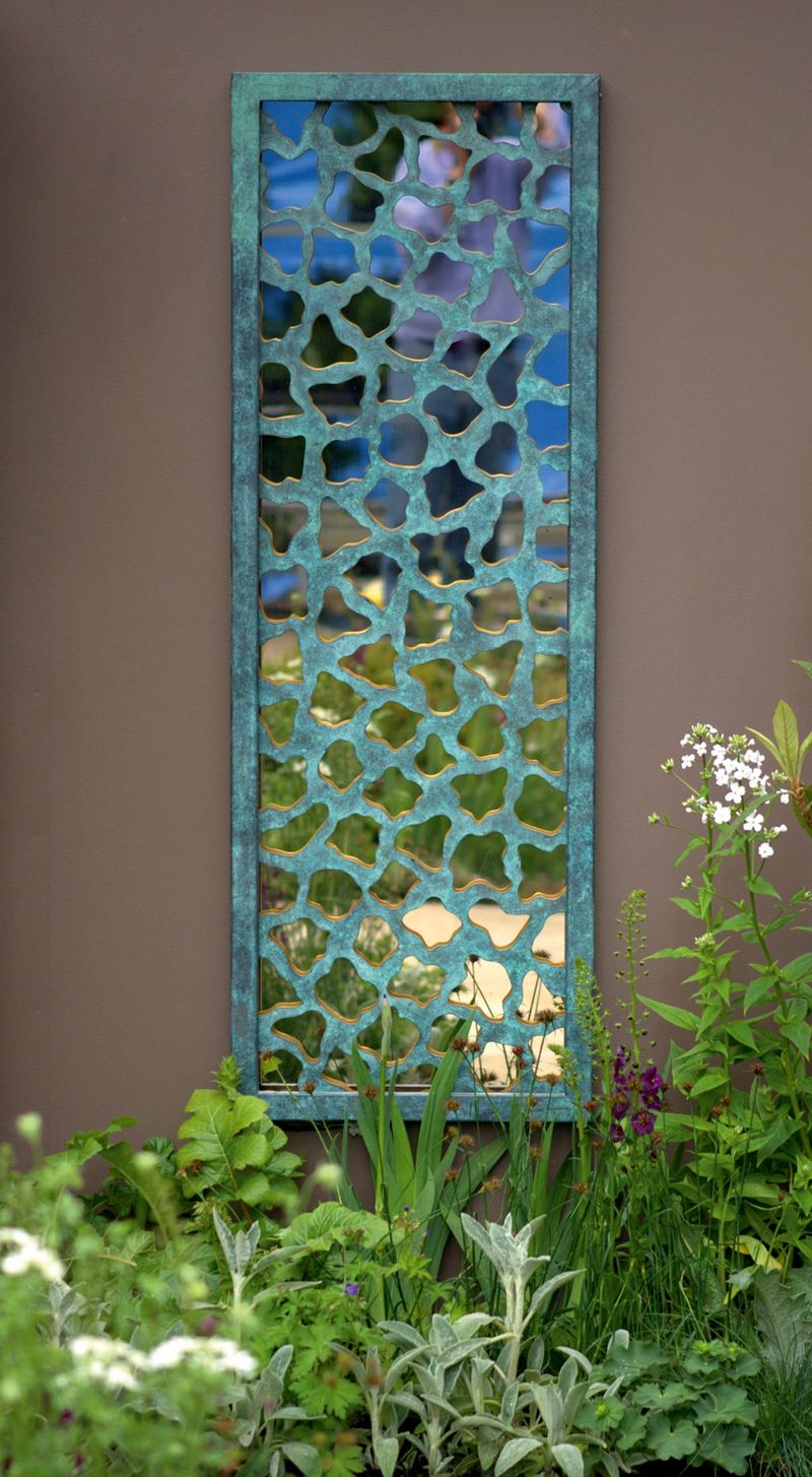 Rectangular patterned mirror on a brown wall reflectin the sky and greenery for that perfect courtyard garden ideas.