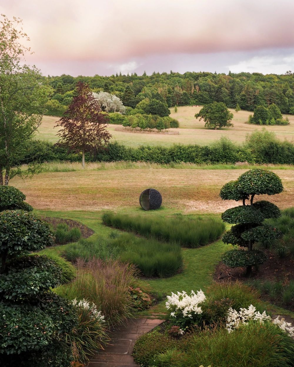landscaped garden with sculpted bushes, white flowers, and an architectural garden design-inspired sculpture