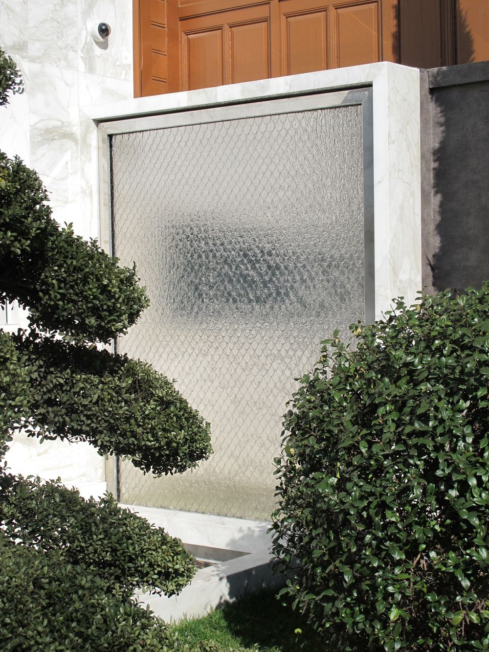 Petal Water Wall in stainless steeloutside a building, accented by bushes and tree