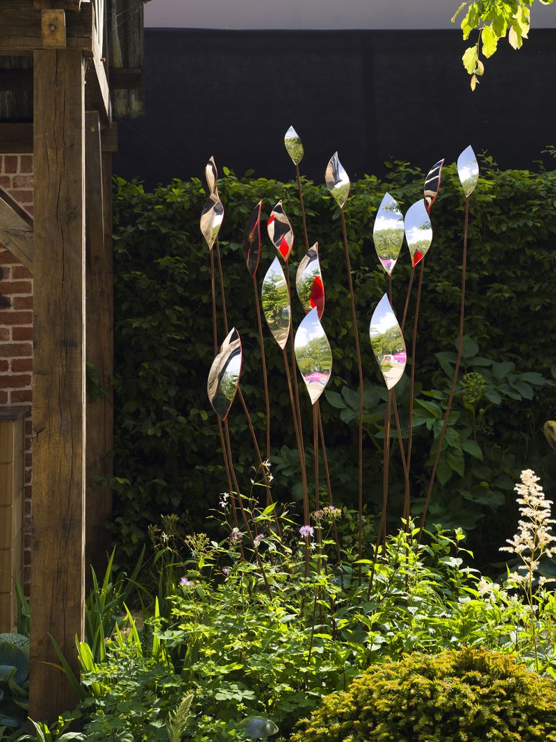 Tall, reflective leaf sculptures add a modern touch among green plants for an inspiring courtyard garden idea