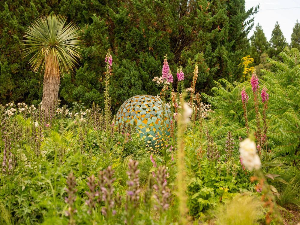 lush architectural garden design featuring tall green plants, pink and white flowers and a decorative sphere