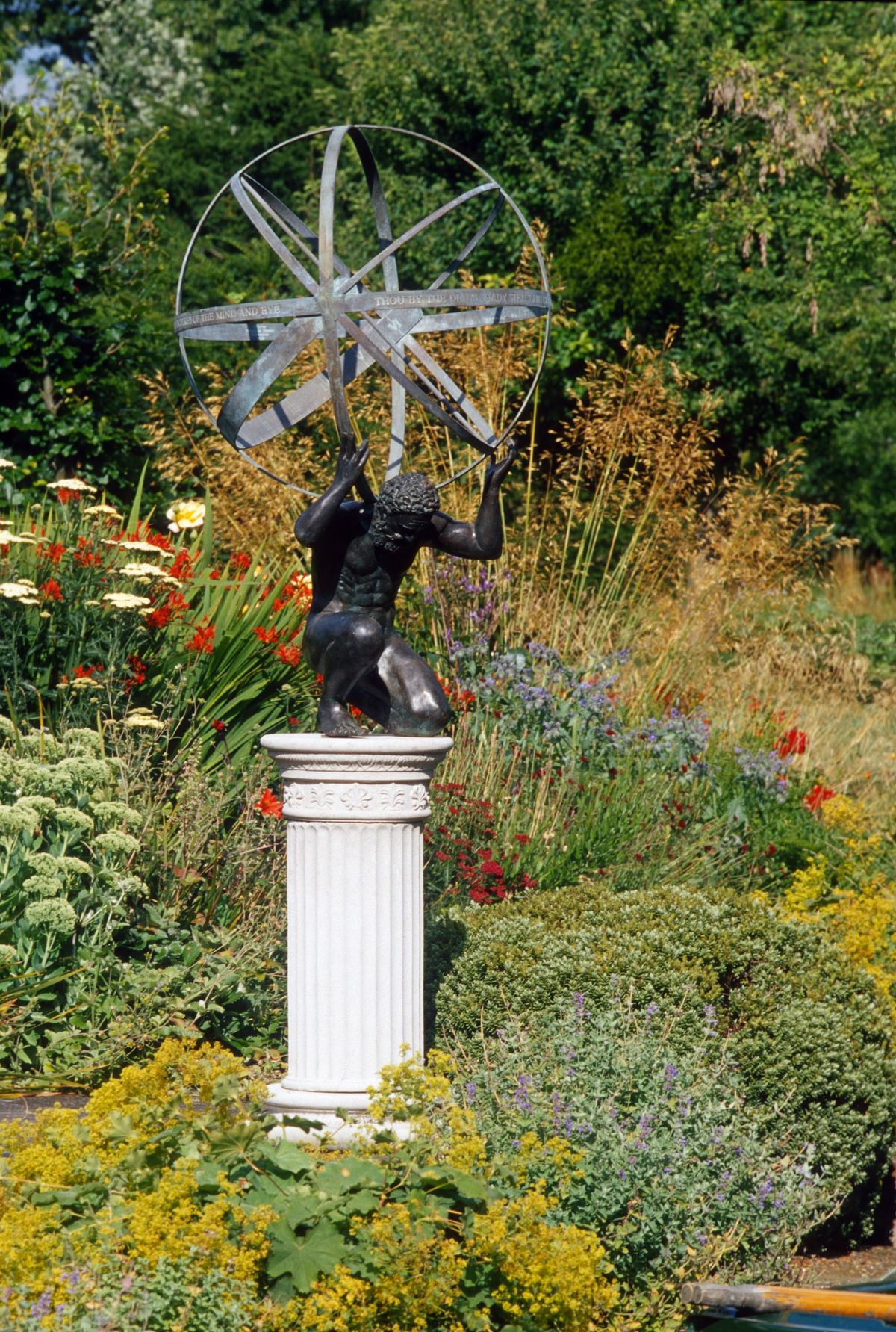 Bronze statue of Atlas holding an armillary sphere atop a white plinth, perfect for unique garden sundial ideas.