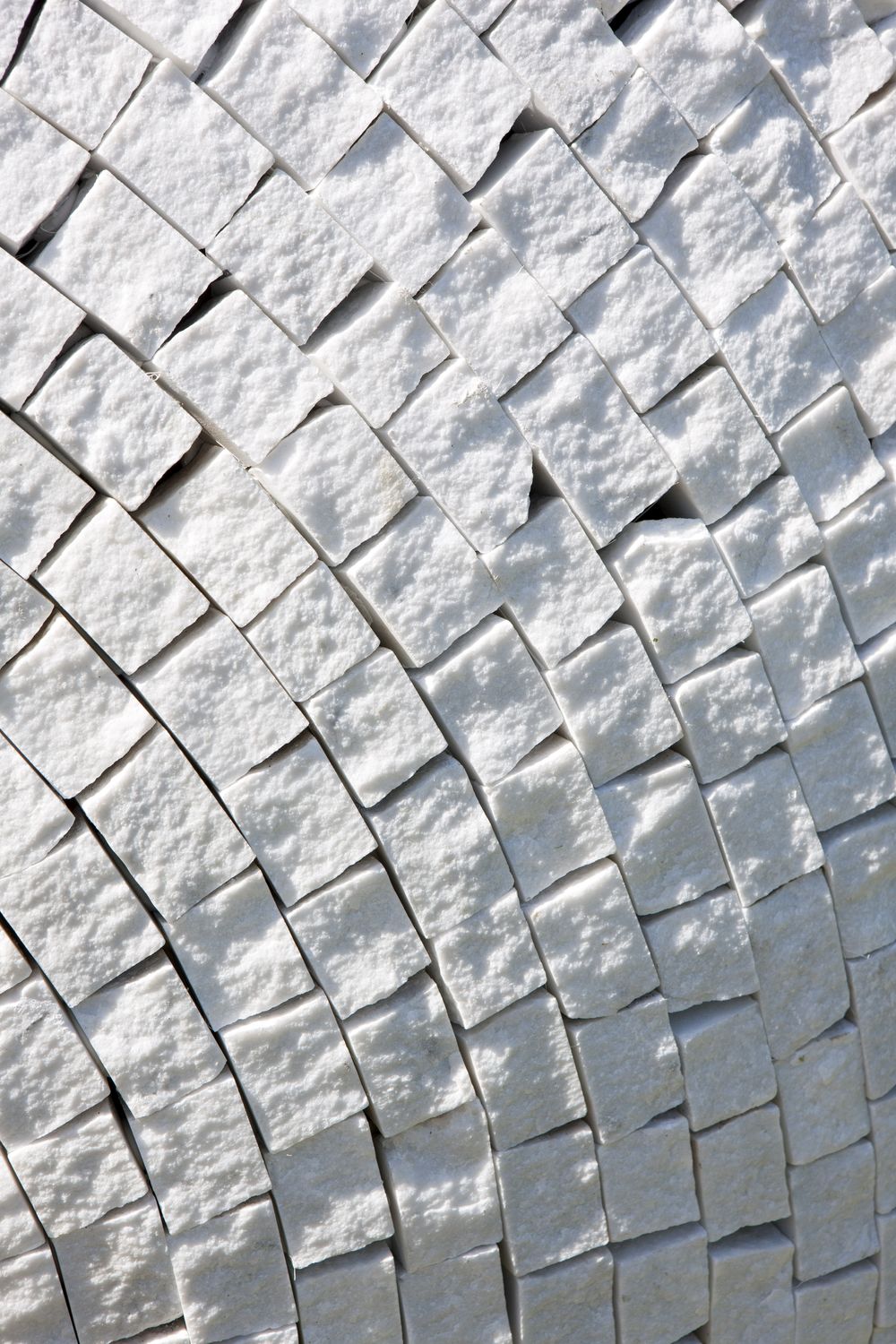 Curved rows of white Carrara marble blocks form a repeating, textured pattern like a torus floor sculpture.