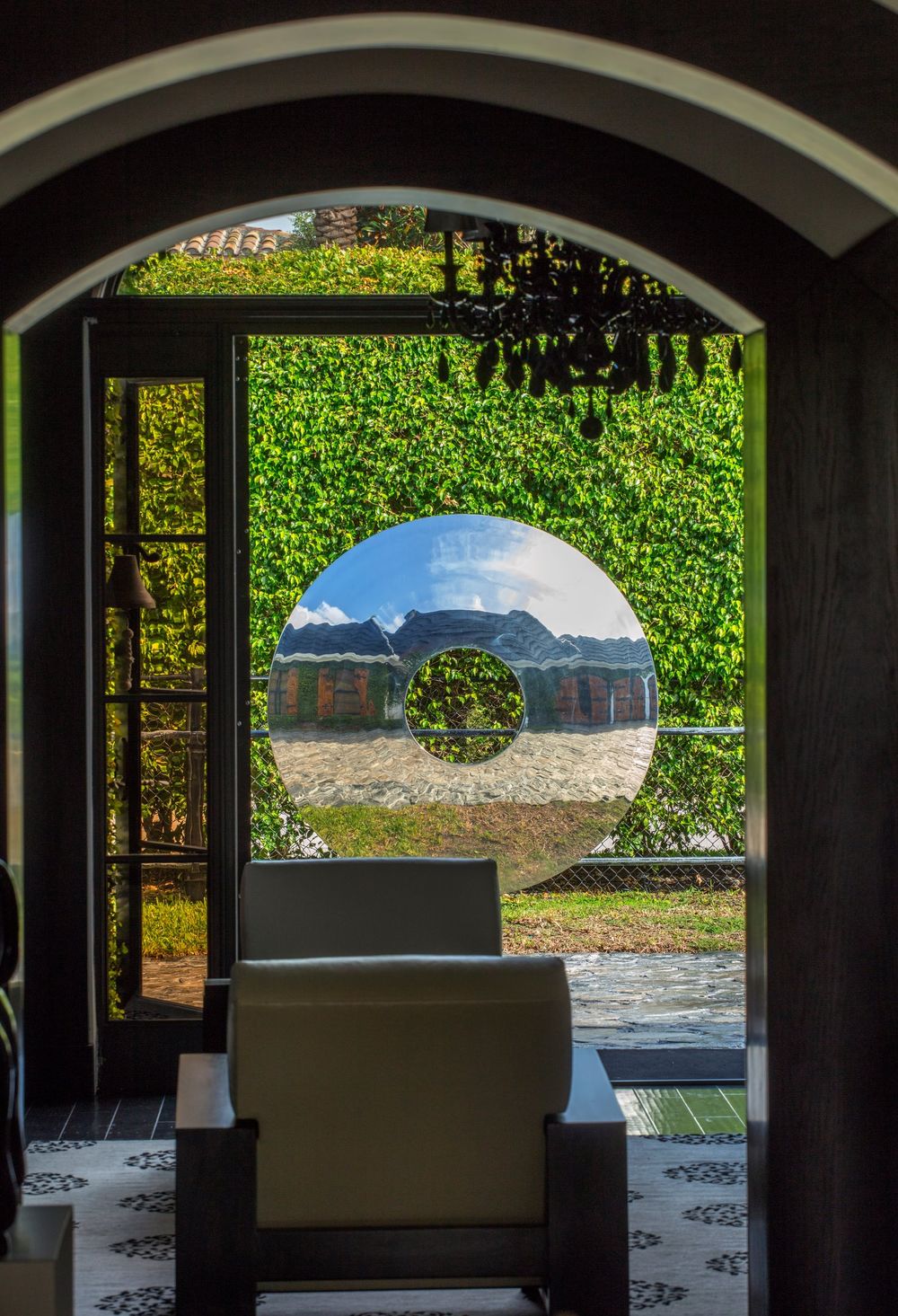 polished, reflective metal sphere sculpture framed by an arched entryway mirroring lush foliage, highlighting garden wall feature ideas