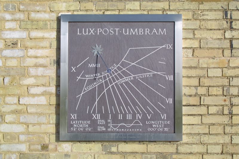 A vertical dial in slate with Roman numerals and solstice markings mounted on a yellow brick wall.