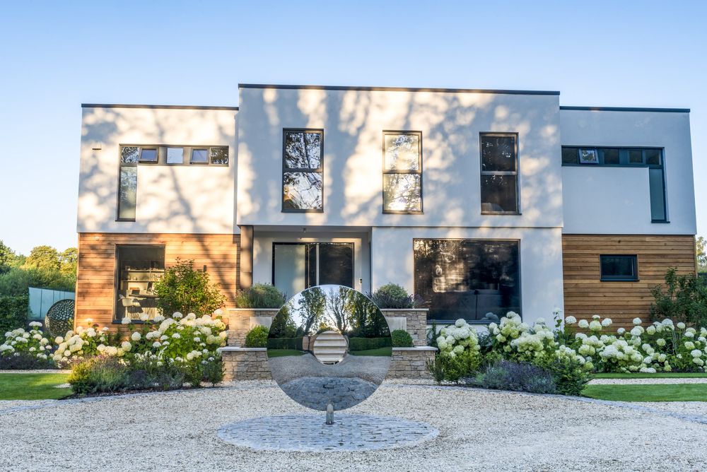 Contemporary house facade highlighting architectural garden designing with a centered stone fire pit and structured walkway shrubbery